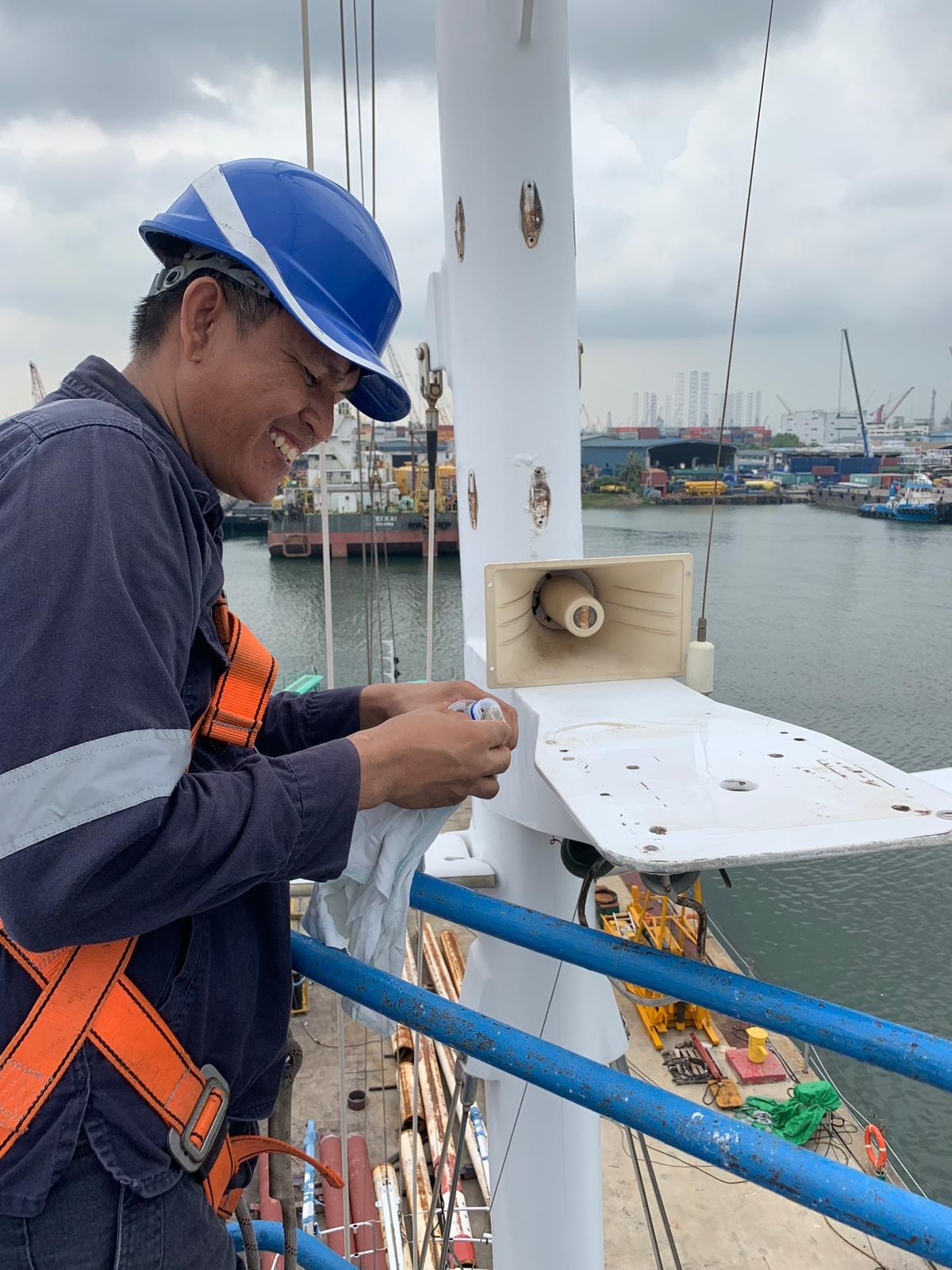 Technician on mast with Singapore port behind during sustainable refit